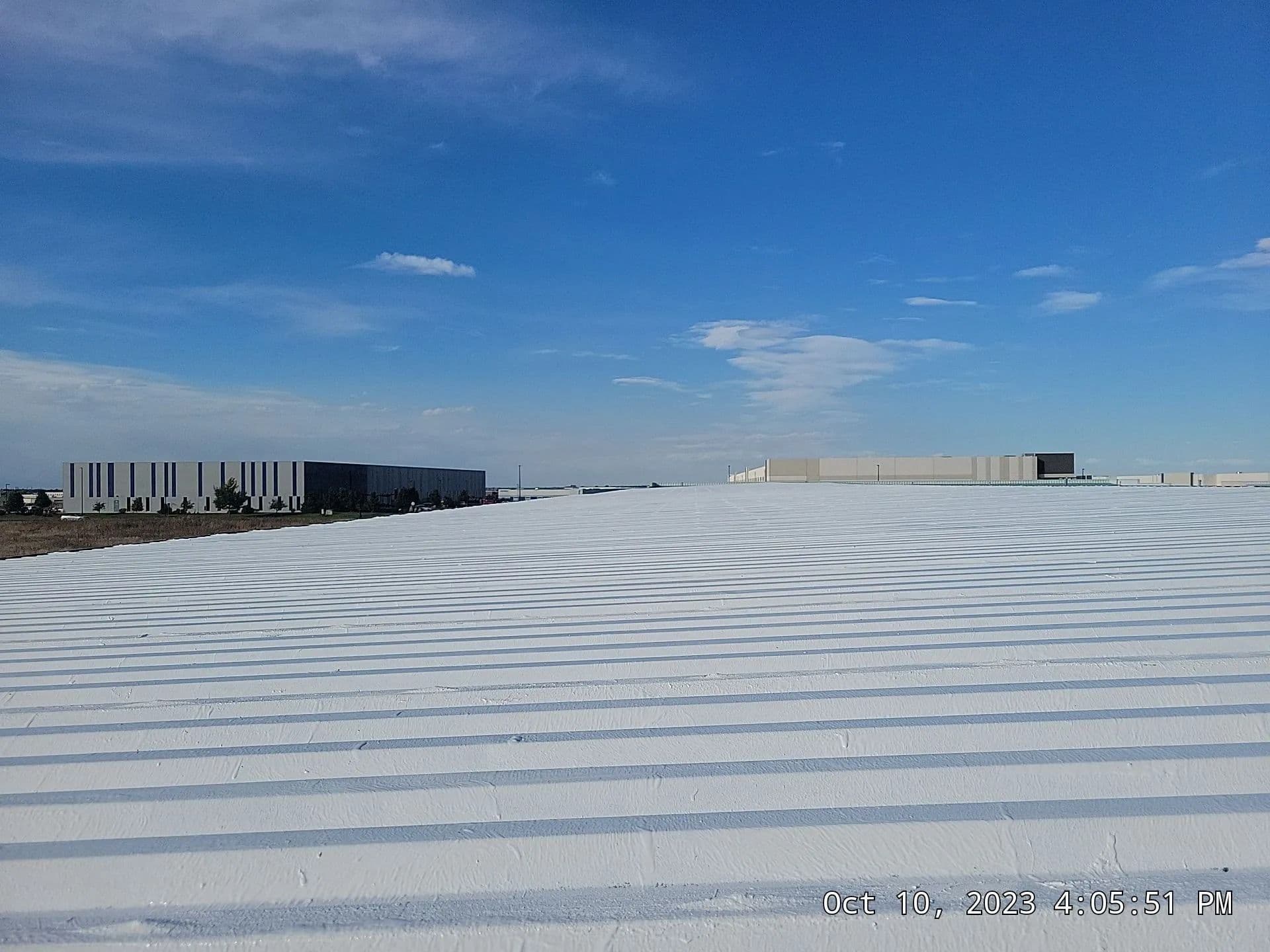 A freshly coated white metal roof stretching toward the horizon under a blue Colorado sky