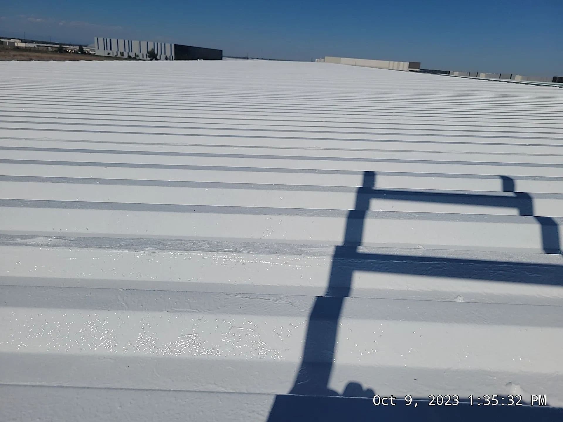 The shadow of a roof ladder across the ribs of a freshly coated commercial roof